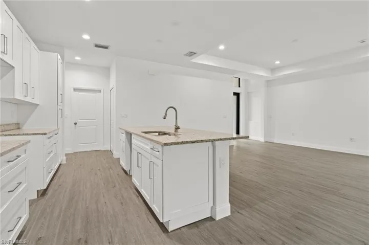 Kitchen featuring light wood-type flooring, white cabinets, light stone counters, a tray ceiling, and sink