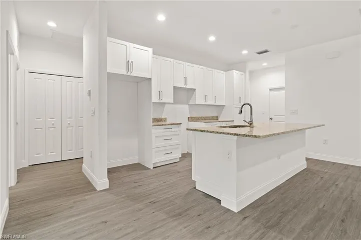 Kitchen with white cabinetry, a center island with sink, light hardwood / wood-style floors, light stone countertops, and sink