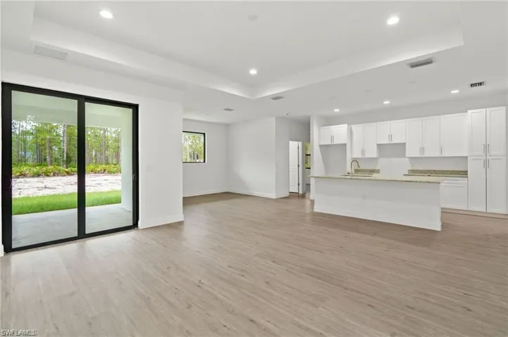 Unfurnished living room with sink, light wood-type flooring, and a tray ceiling