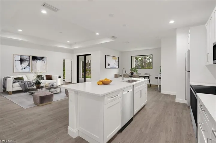 Kitchen featuring white cabinets, light hardwood / wood-style flooring, appliances with stainless steel finishes, and an island with sink