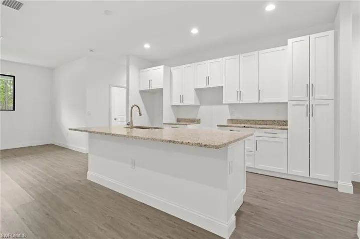 Kitchen with white cabinets, light hardwood / wood-style flooring, sink, and an island with sink
