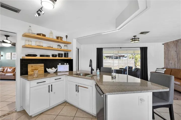 Kitchen featuring open shelves, light stone countertops, white cabinetry, light tile patterned floors, and a breakfast bar