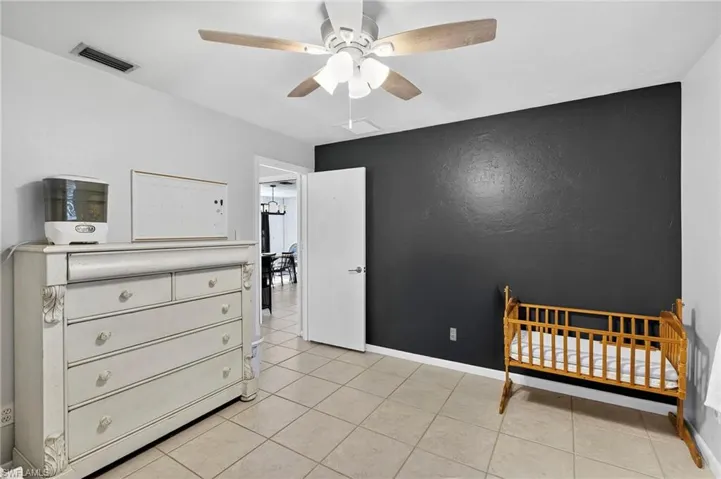 Bedroom with light tile patterned floors, a crib, and ceiling fan