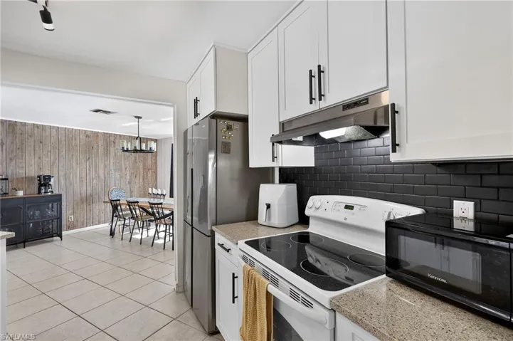 Kitchen with white electric range oven, black microwave, under cabinet range hood, white cabinets, and wooden walls