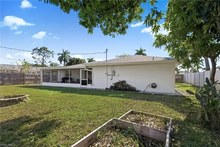 Rear view of property with a vegetable garden, a fenced backyard, an outdoor fire pit, a sunroom, and stucco siding