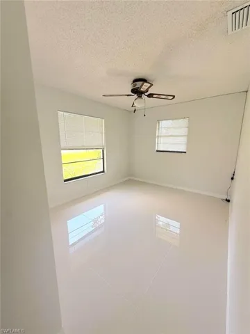 Empty room with a textured ceiling, tile patterned floors, and ceiling fan