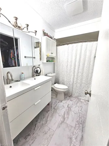Bathroom with marble look tile flooring, toilet, vanity, a textured ceiling, and curtained shower