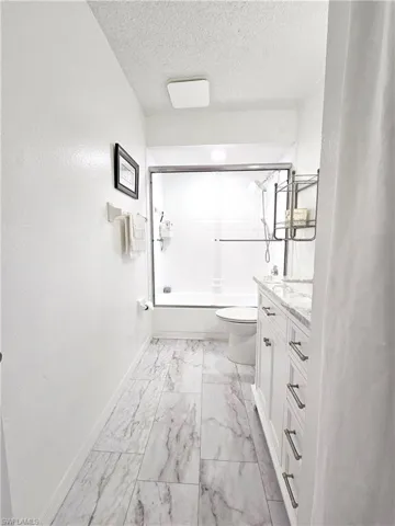 Full bathroom with marble look tile flooring, baseboards, toilet, vanity, and shower / bath combination with glass door