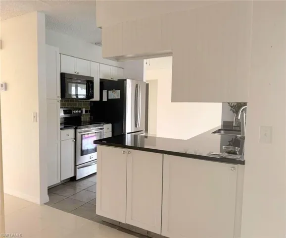 Kitchen featuring appliances with stainless steel finishes, light tile patterned flooring, white cabinets, a peninsula, and decorative backsplash