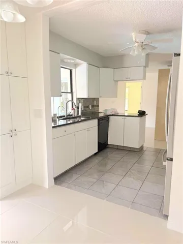 Kitchen featuring light tile patterned floors, white cabinets, a textured ceiling, freestanding refrigerator, and black dishwasher