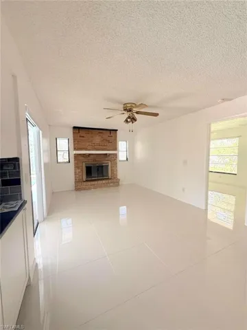 Unfurnished living room featuring light tile patterned floors, a ceiling fan, a textured ceiling, plenty of natural light, and a brick fireplace