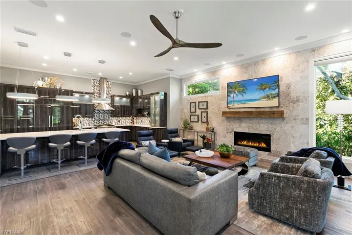 Living room featuring crown molding, a large fireplace, a ceiling fan, dark wood-type flooring, and recessed lighting