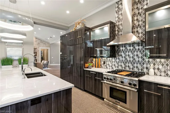 Kitchen featuring light stone counters, premium appliances, dark wood finish cabinets, modern cabinets, and crown molding