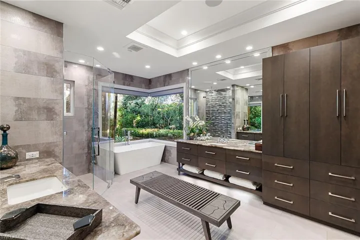 Full bath with a stall shower, two vanities, a soaking tub, tile walls, and recessed lighting