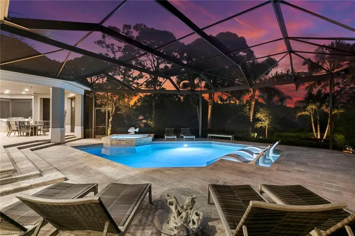 Pool at dusk featuring a pool with connected hot tub, a lanai, outdoor dining area, a patio, and a sunroom