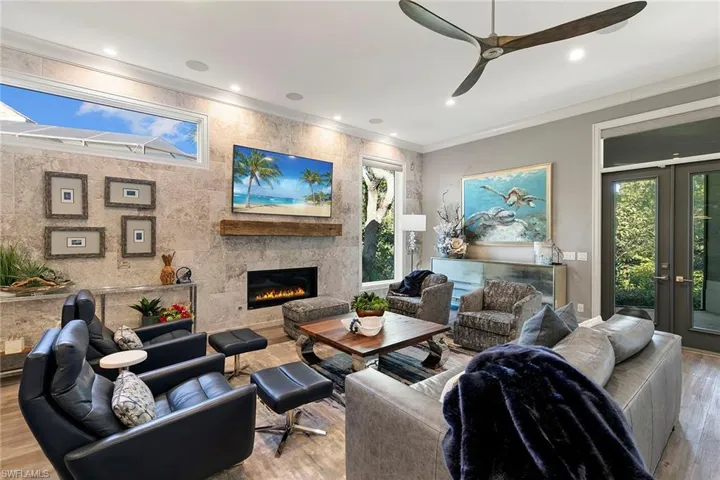 Living room with wood finished floors, crown molding, french doors, a large fireplace, and ceiling fan