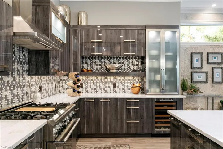 Bar area featuring high end stainless steel range oven, dark wood finish cabinetry, wine cooler, light stone countertops, and glass fronted cabinets