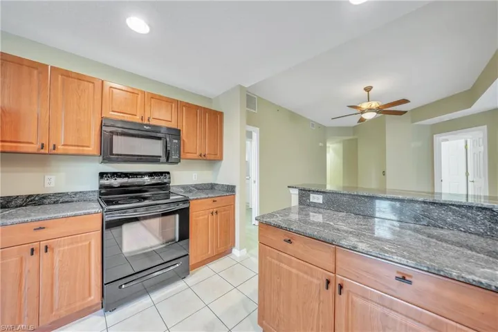 Kitchen featuring black appliances, dark stone counters, light tile patterned floors, ceiling fan, and brown cabinets