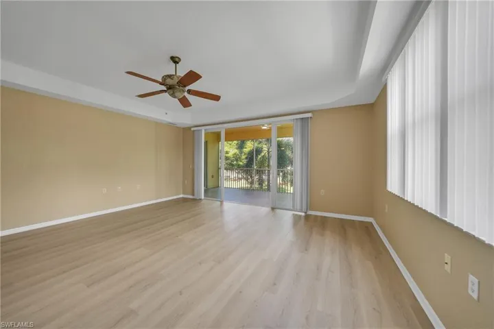 Empty room with light wood-type flooring, expansive windows, ceiling fan, and a raised ceiling