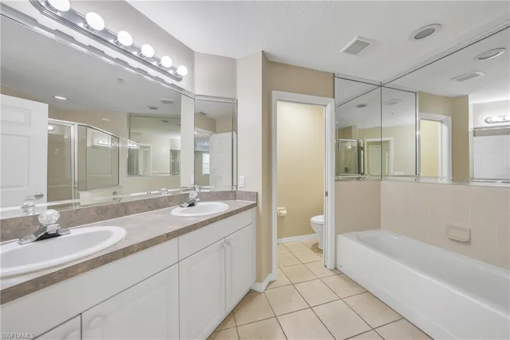 Bathroom with double vanity, light tile patterned floors, a textured ceiling, a bath, and a shower stall