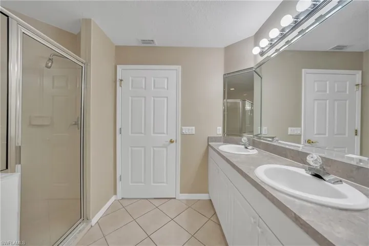 Full bathroom with light tile patterned floors, double vanity, a textured ceiling, and a stall shower