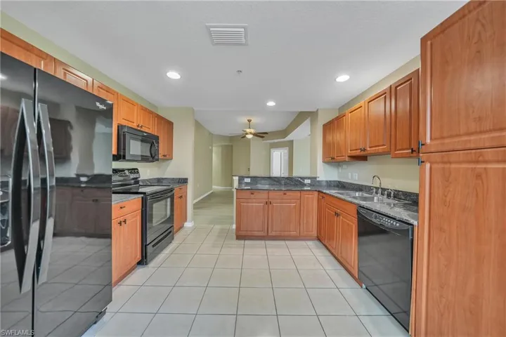 Kitchen featuring black appliances, dark stone counters, a peninsula, recessed lighting, and light tile patterned floors