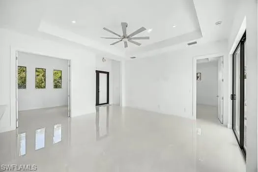 Unfurnished room with finished concrete floors, ceiling fan, and a tray ceiling