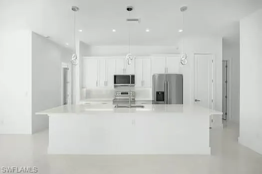 Kitchen with white cabinets, stainless steel appliances, a spacious island, hanging light fixtures, and light stone countertops