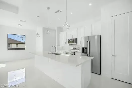 Kitchen with stainless steel appliances, white cabinets, pendant lighting, an island with sink, and finished concrete flooring