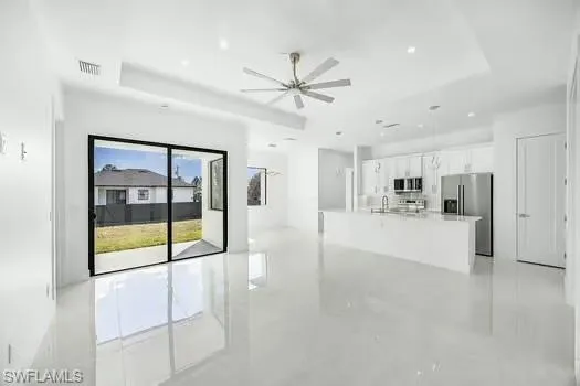 Unfurnished living room featuring a ceiling fan, a raised ceiling, and finished concrete floors