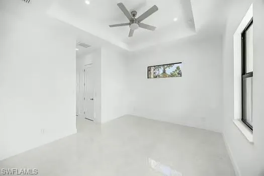 Unfurnished room with finished concrete floors, a tray ceiling, and ceiling fan