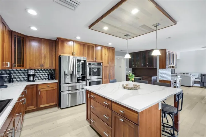 Kitchen with brown cabinets, glass insert cabinets, stainless steel appliances, light stone countertops, and recessed lighting