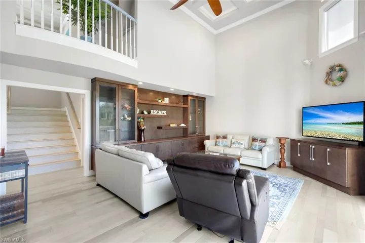 Living area with a ceiling fan, light wood-style floors, a towering ceiling, and stairs