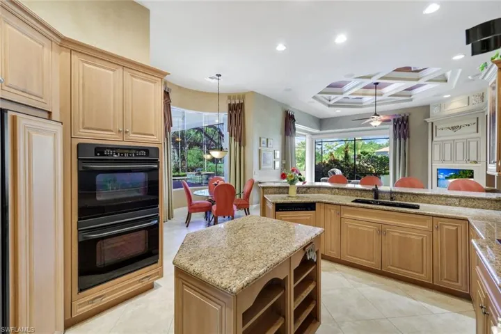 Kitchen featuring light stone counters, coffered ceiling, a kitchen island, black double oven, and ceiling fan