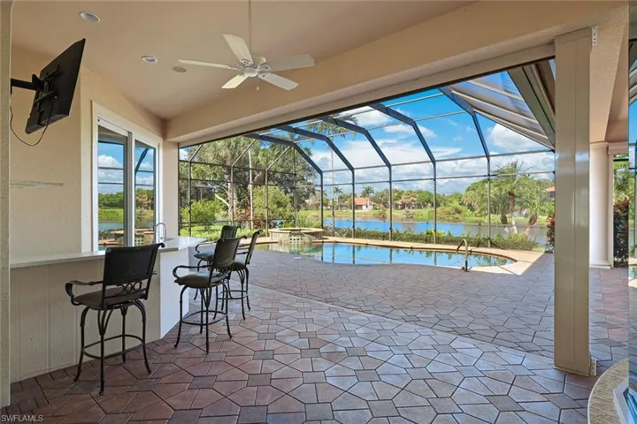 View of patio featuring ceiling fan, a water view, an outdoor bar, and a lanai