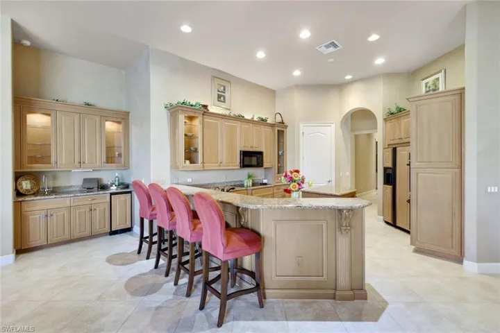 Kitchen with light stone counters, light brown cabinets, paneled built in fridge, a kitchen breakfast bar, and a center island