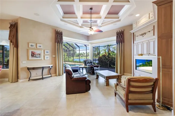 Living room featuring beam ceiling, coffered ceiling, light tile patterned floors, ornamental molding, and ceiling fan