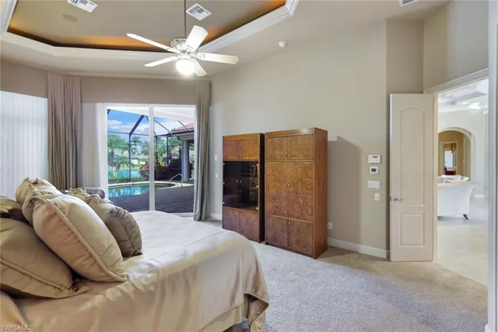 Carpeted bedroom featuring a raised ceiling, crown molding, ceiling fan, and access to exterior