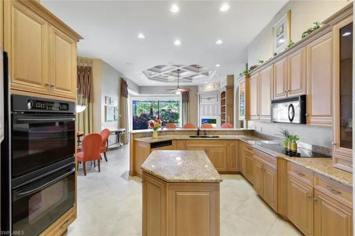 Kitchen with light stone counters, kitchen peninsula, black appliances, a center island, and ceiling fan