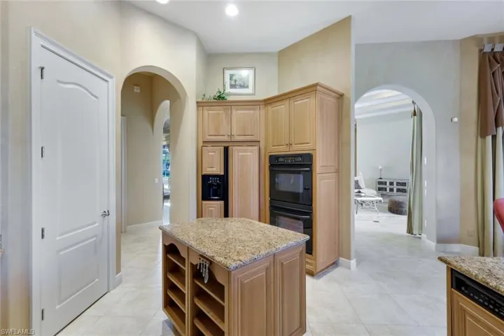 Kitchen with light stone counters, light tile patterned floors, a kitchen island, and black double oven