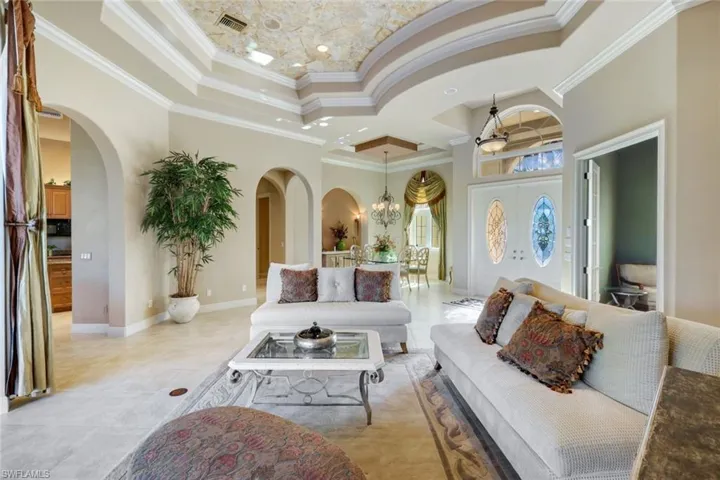 Living room with crown molding, a high ceiling, ceiling fan with notable chandelier, and light tile patterned floors