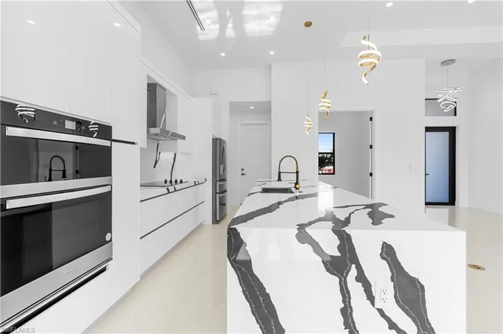 Kitchen featuring wall chimney range hood, a sink, modern cabinets, double oven, and freestanding refrigerator
