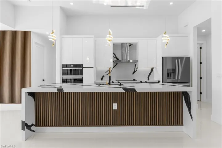 Kitchen featuring dobule oven black, wall chimney range hood, stainless steel refrigerator with ice dispenser, and modern cabinets