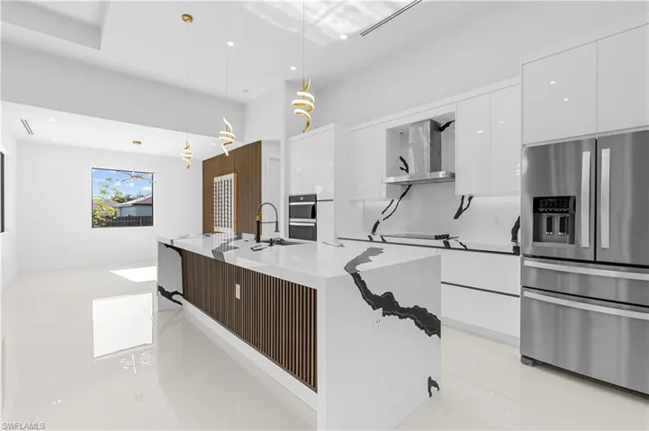 Kitchen featuring wall chimney exhaust hood, modern cabinets, stainless steel fridge, and white cabinetry