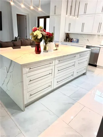 Kitchen featuring dishwasher, light marble finish floors, light stone countertops, white cabinets, and open floor plan