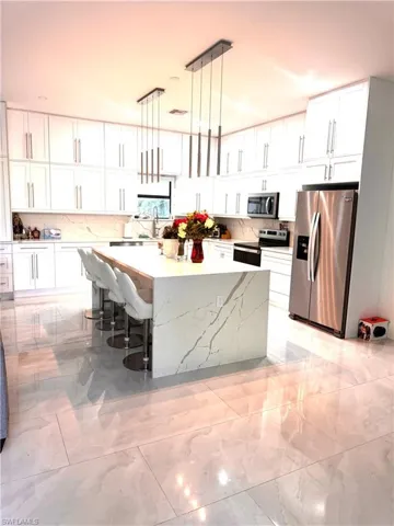 Kitchen featuring stainless steel appliances, a kitchen island, light marble finish flooring, and white cabinetry