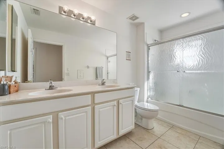 Full bathroom featuring double vanity, light tile patterned floors, and bath / shower combo with glass door