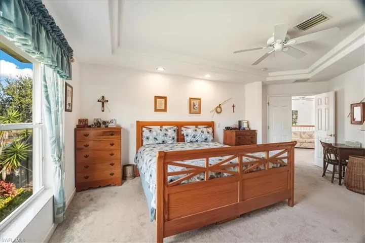 Bedroom with a raised ceiling, light colored carpet, ceiling fan, and recessed lighting