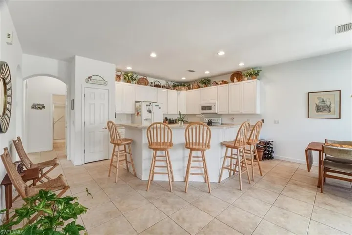 Kitchen with a breakfast bar, arched walkways, white appliances, white cabinets, and light tile patterned flooring