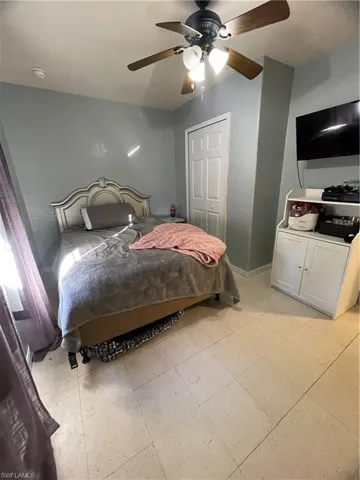 Room featuring light-toned square-tile flooring, a window with sheer purple drapery, and a ceiling fan with integrated lighting